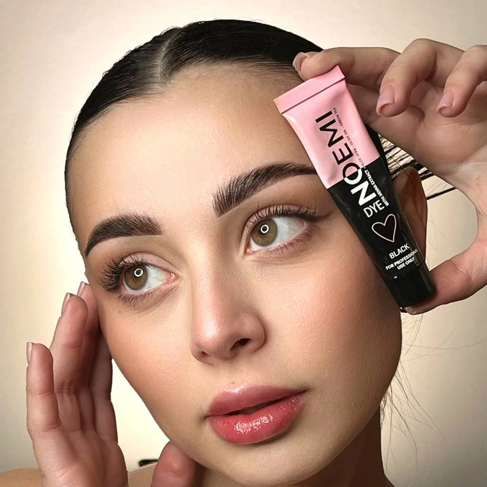 Person holding a makeup product near their face with a neutral background